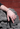 A close-up of a person's hand resting on a carved stone sculpture, wearing a silver-toned beaded bracelet on one wrist and multiple silver rings on the fingers, with a red brick wall in the background.