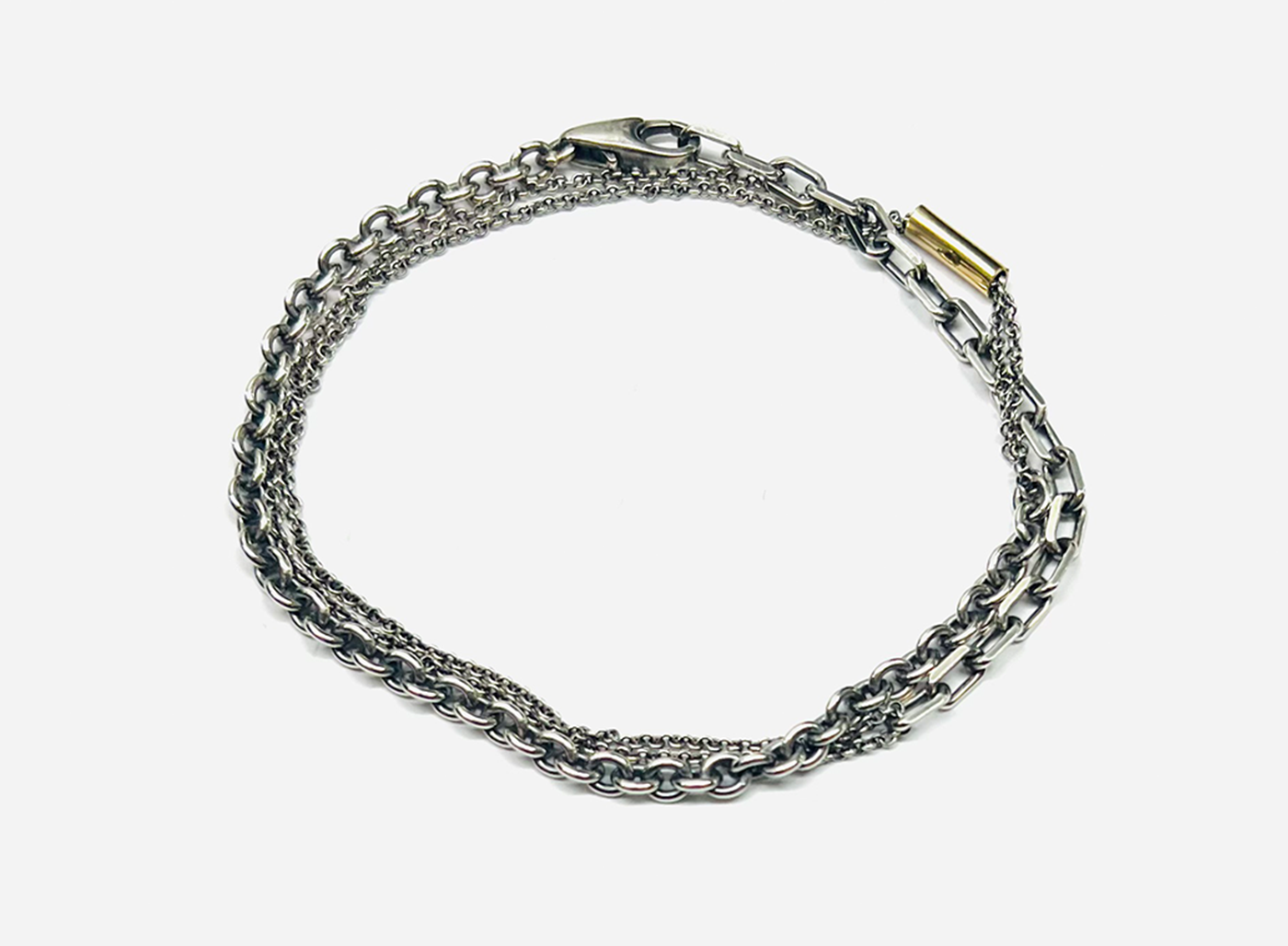 bracelet is comprised of three separate chains including a thin double strand cable chain, more dense single strand cable chain and an anchor chain, accented by an 18k yellow gold tube