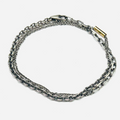 bracelet is comprised of three separate chains including a thin double strand cable chain, more dense single strand cable chain and an anchor chain, accented by an 18k yellow gold tube