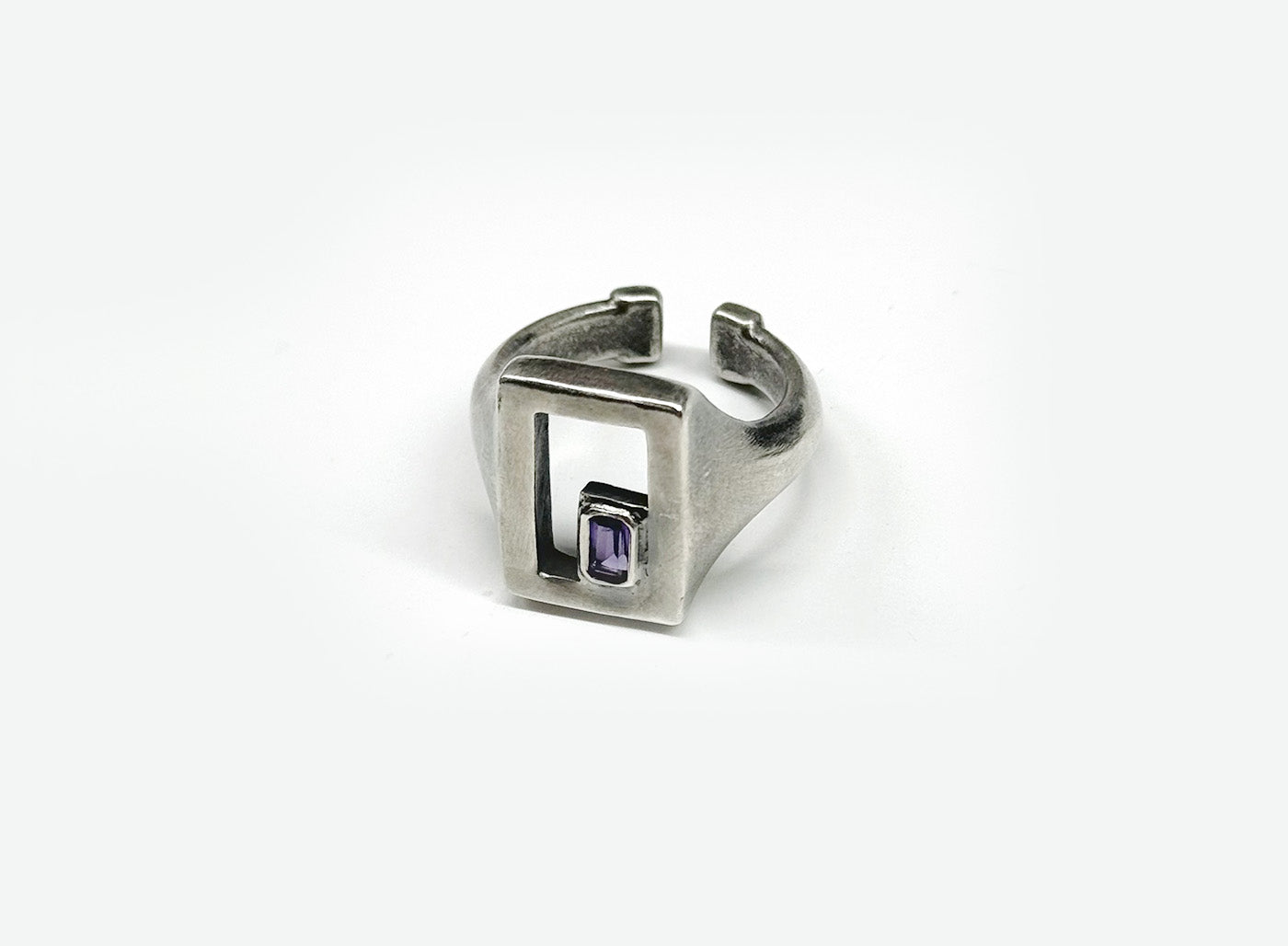 a single emerald-cut amethyst gemstone sits elegantly framed in the corner of an open face sterling silver signet ring that distressed and hand finished